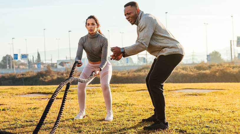 Personal trainer helping a client outside in the park using ropes