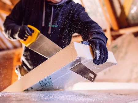 A handyman sawing through insulation in an attic