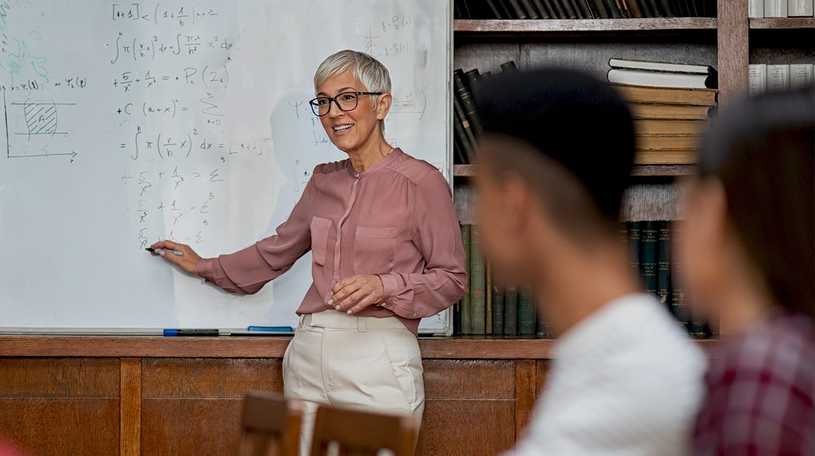 Female teacher standing at chalk board in front of a class of students