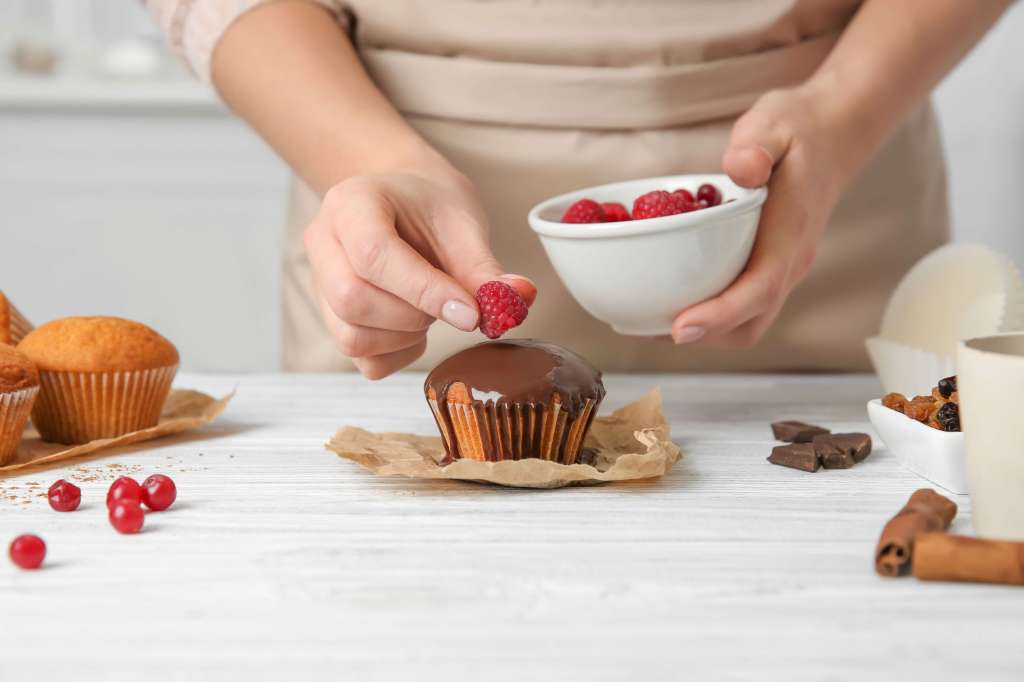 Baker decorating cupcakes with raspberries for selling from home