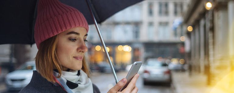 A woman looking at her phone while holding an umbrella