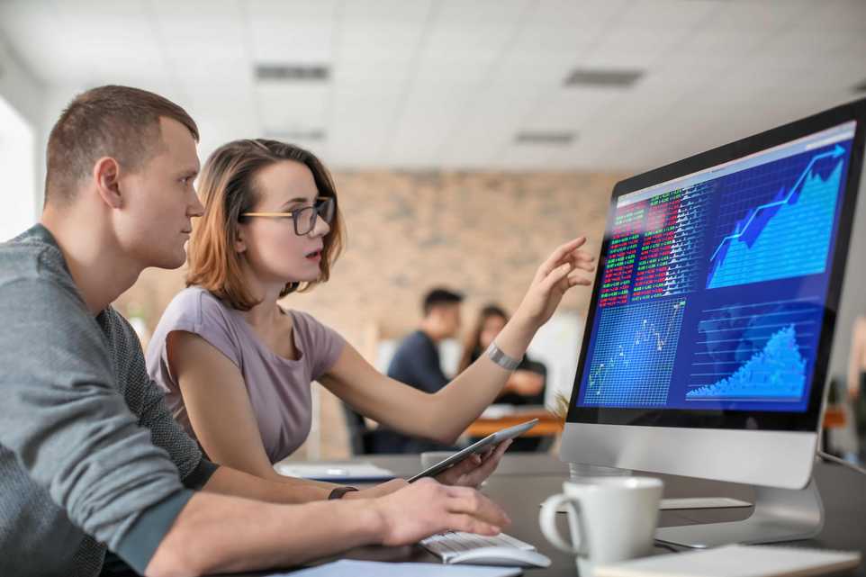 Two people reviewing stock market on computer screen
