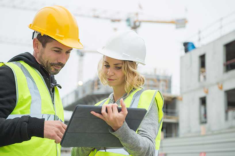 Two builders in hardhats with tablet at construction site