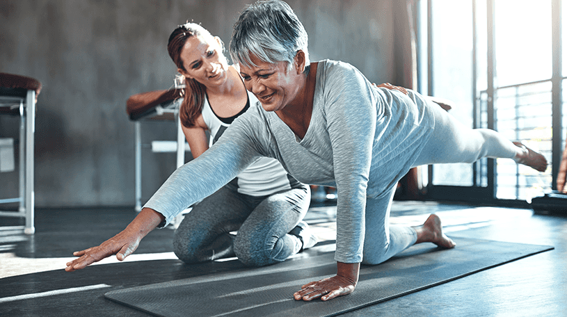Fitness instructor helping an elderly client in a gym