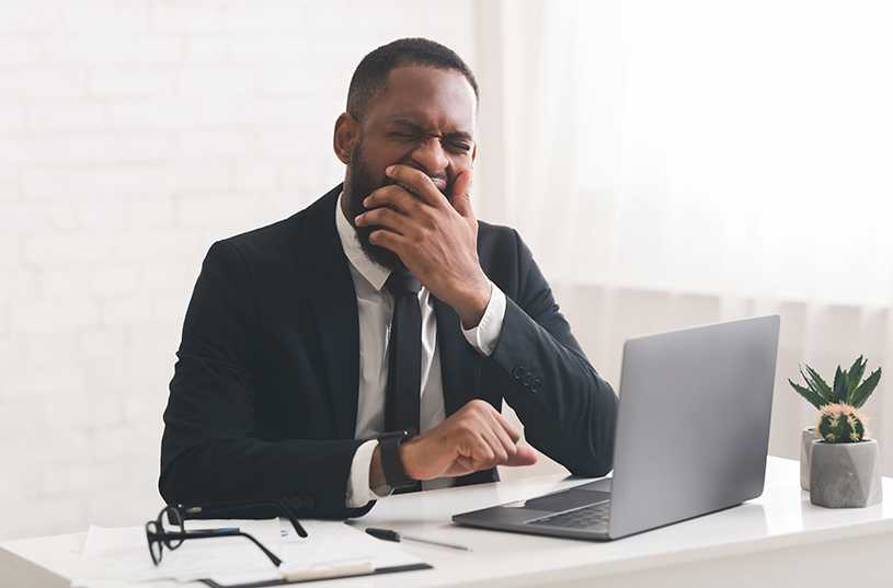 Businessman yawning at a desk with laptop
