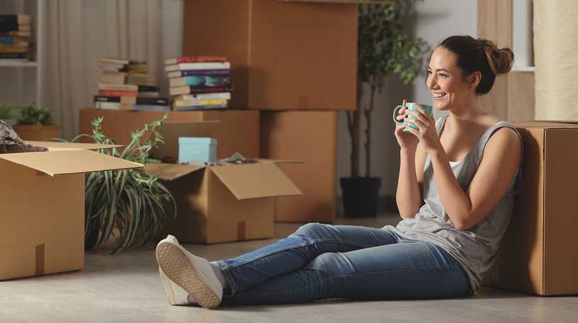 Woman having a hot drink sitting next to moving boxes