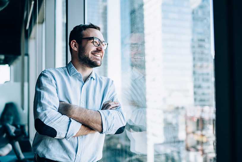 Smiling man in glasses looking out of an office window