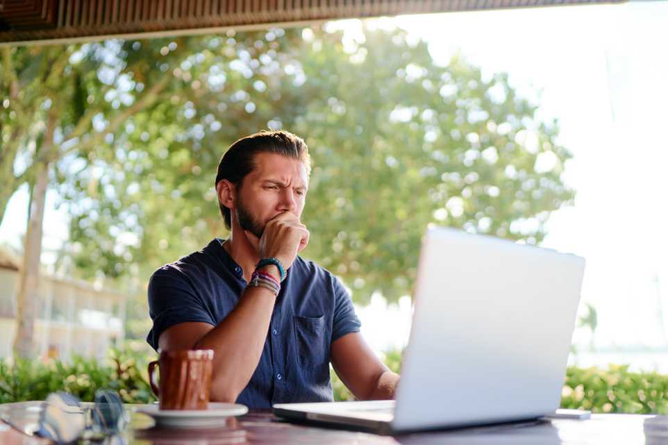 Serious man looking at laptop on sunny terrace