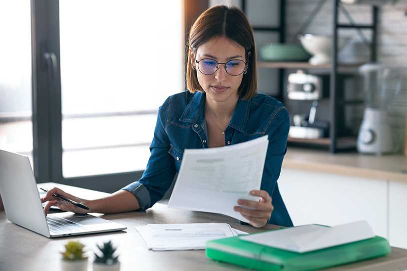 Businesswoman wearing glasses looking at paperwork with laptop