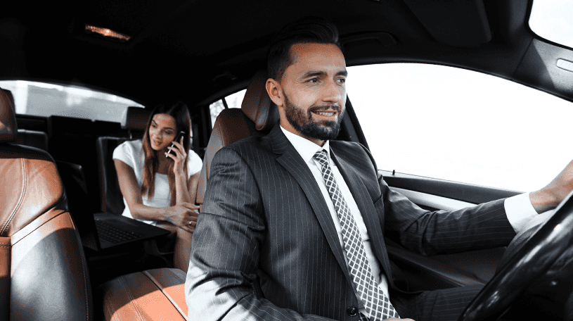 Chauffeur driving a car with a female passenger on her phone