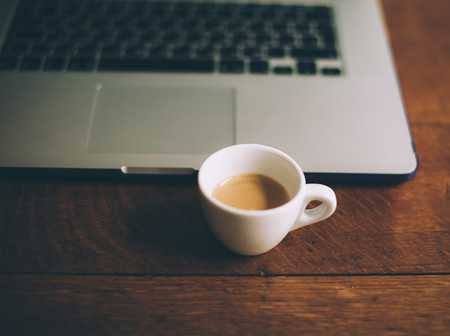 Small cup of coffee next to a laptop on a desk