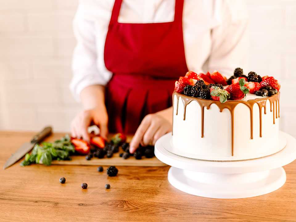 Baker decorating white cake with fresh berries