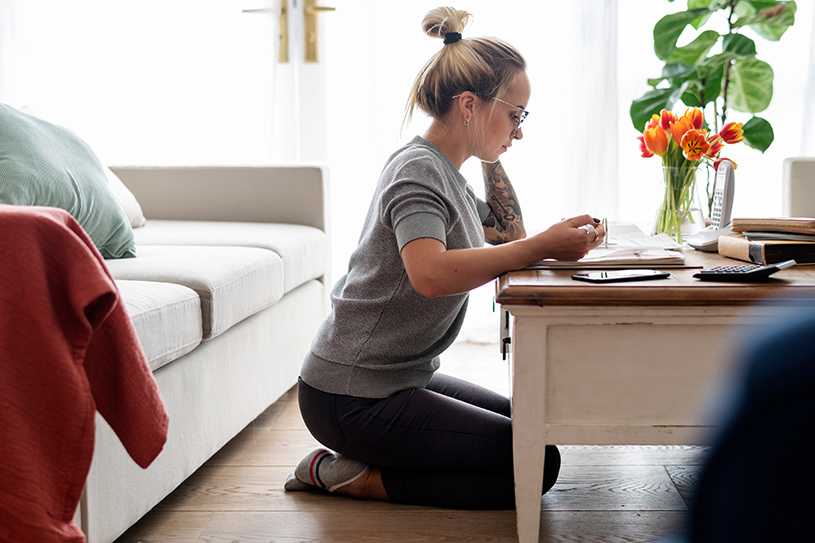 Woman kneeling next to coffee table looking at finances