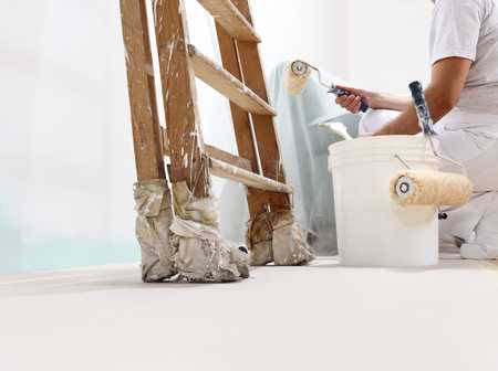 Decorator painting a wall with a foam roller next to his ladder