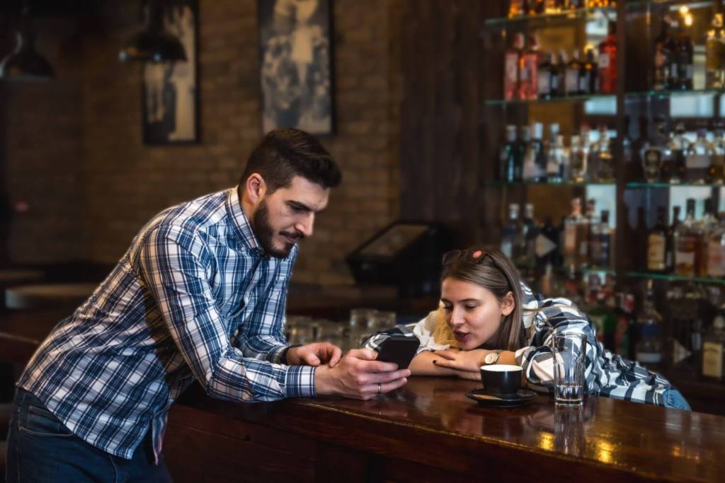 Two barista bartender or waiter workers woman and man working in bar standing and talking, having fun while there is no guests. cafeteria colleagues working and standing at bar counter communicating.