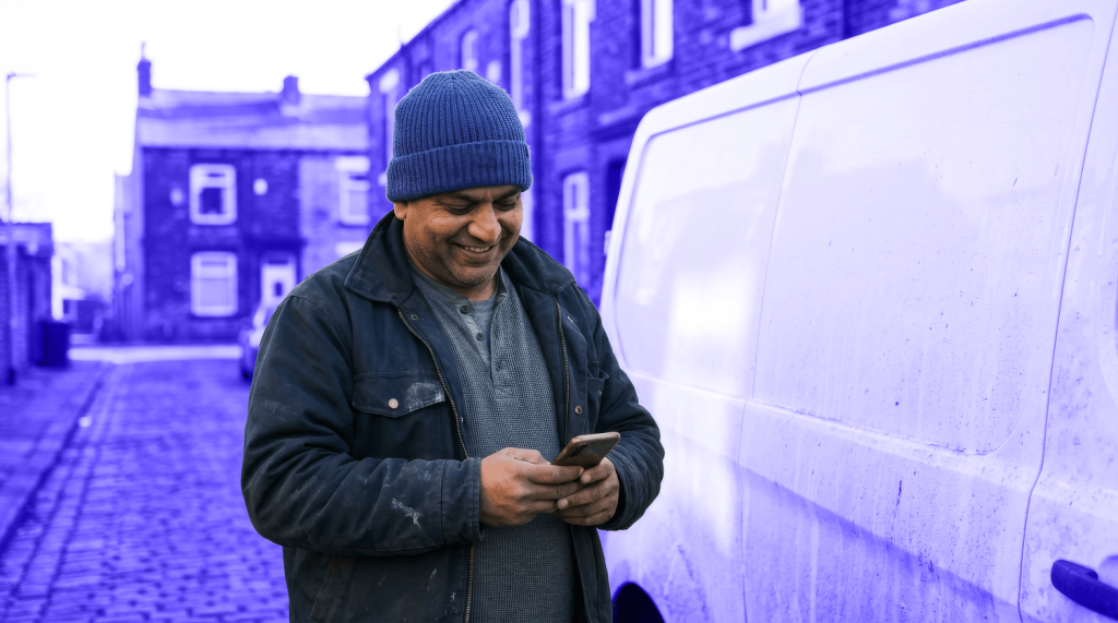 A small business owner looks at his phone while standing by his business van
