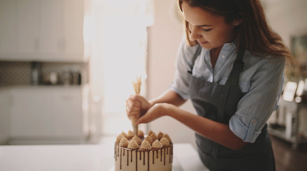 Cake decorator piping icing on the top of a finished cake in the kitchen