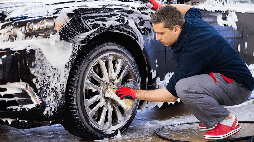 Car valeter washing the wheels on a black car