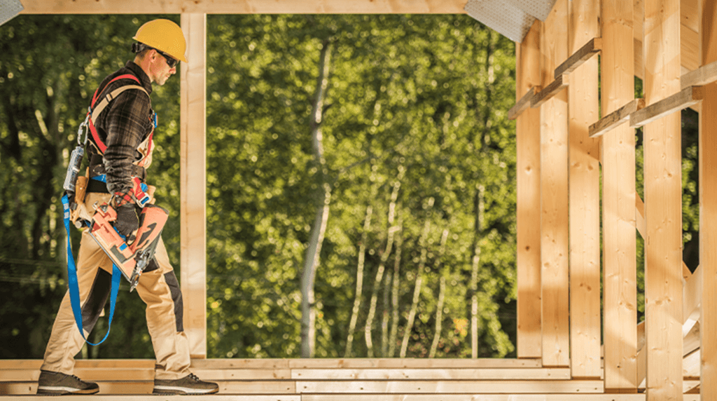 A construction worker walking across roof joists