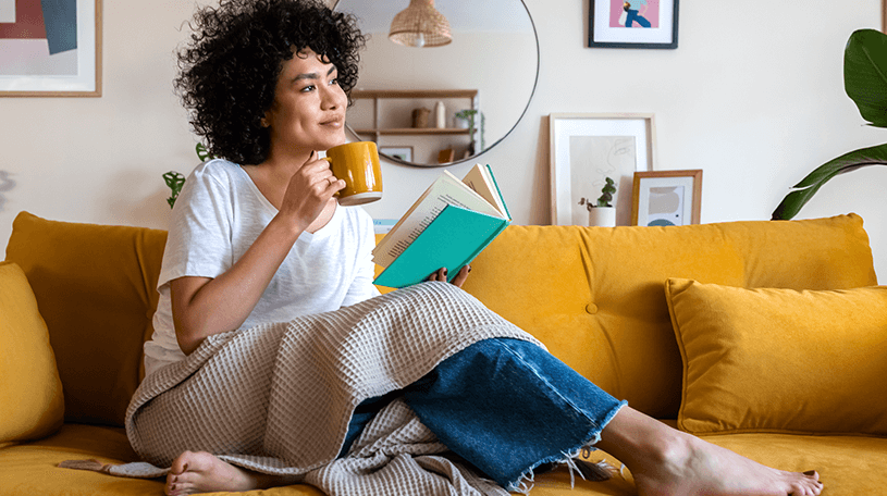 A house sitter sat on the sofa reading a book