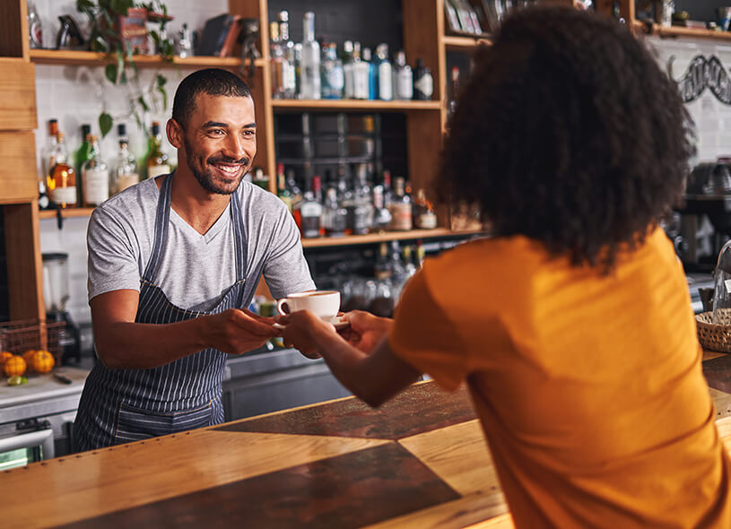 Smiling barista serving coffee to woman in a cafe