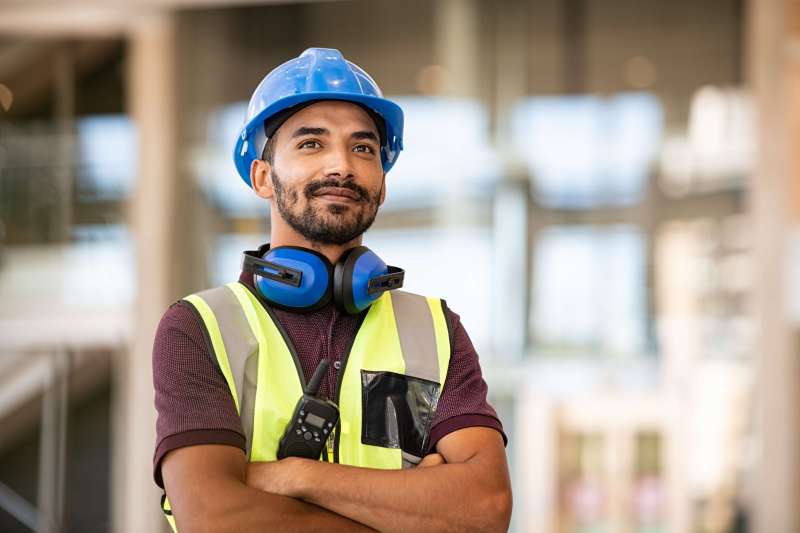 Small business owner wearing PPE including blue hat crosses arms