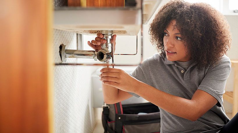 Young female plumber tradesperson working under the sink