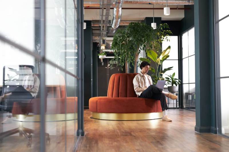 Young man with laptop in seating area of office.