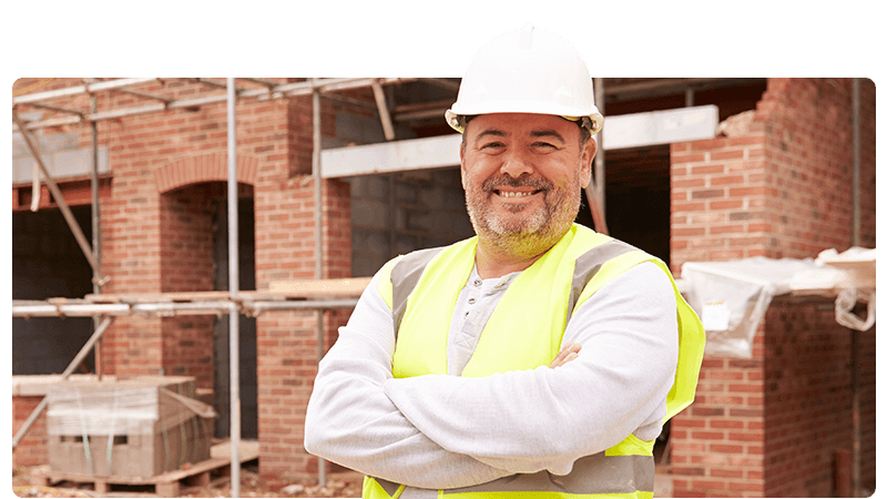 Builder in a hard hat and high viz vest stood on a construction site.