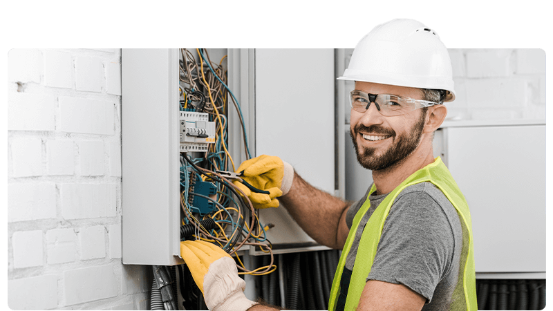 Electrician smiling at the camera whilst fixing wires in a fuse box