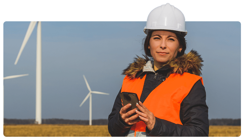 Environmental consultant in a high viz and hard hat in front of wind turbines.