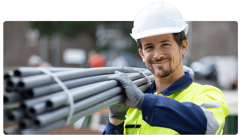 Labourer in a white hard hat carrying pipes