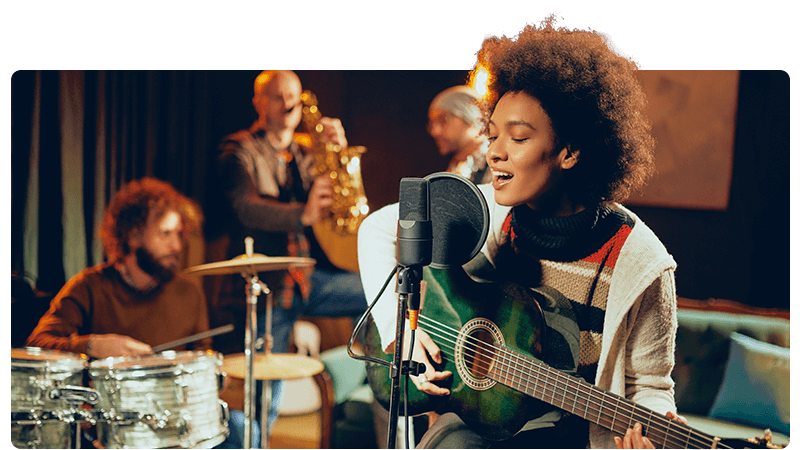 A musician playing the guitar and singing in front of other band members.