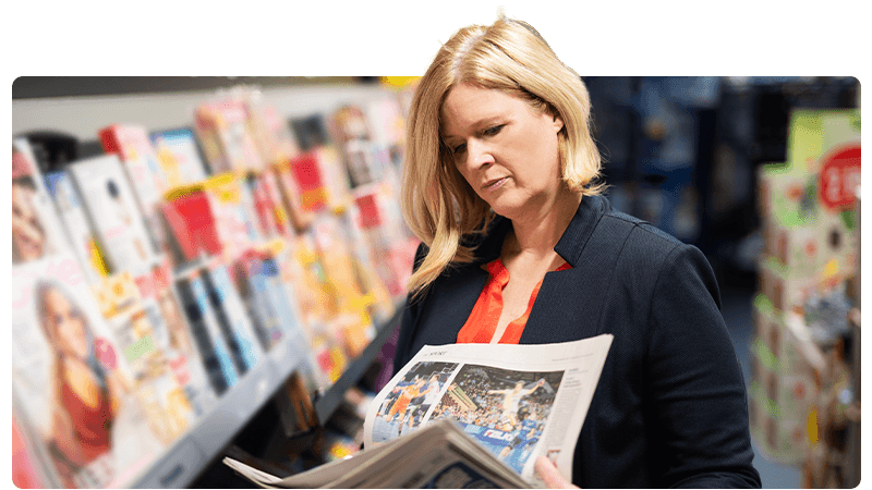 Newsagent with a newspaper in front of a magazine stand