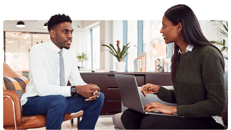 A man being interviewed by a woman with a laptop in a recruitment agency