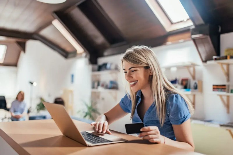 Female small business owner smiles at laptop holding credit card