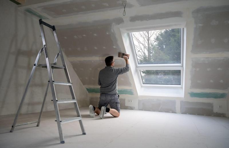 A self-employed decorator plasters drywall in an empty house