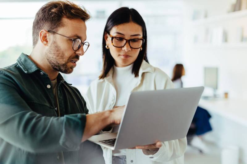 A man and a woman look at a laptop together while working