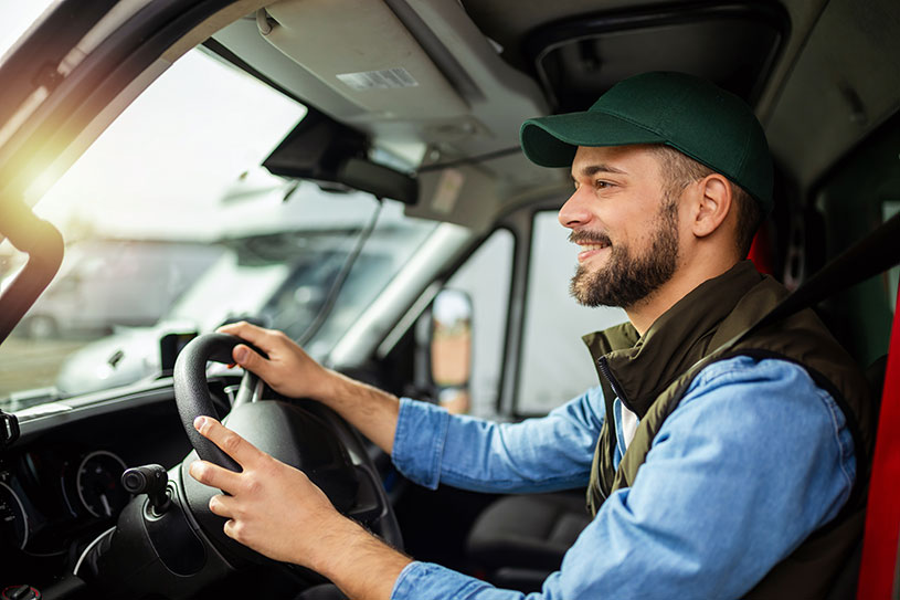 Smiling man driving a van and wearing a baseball hat