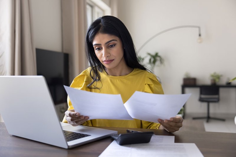 Woman looking at receipts in order to digitally submit her income tax report on a laptop