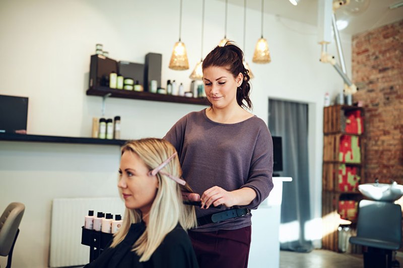 Hairdresser styling blonde woman's hair in salon