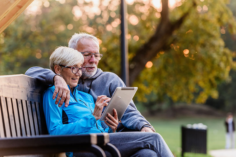Senior couple using a tablet on a bench