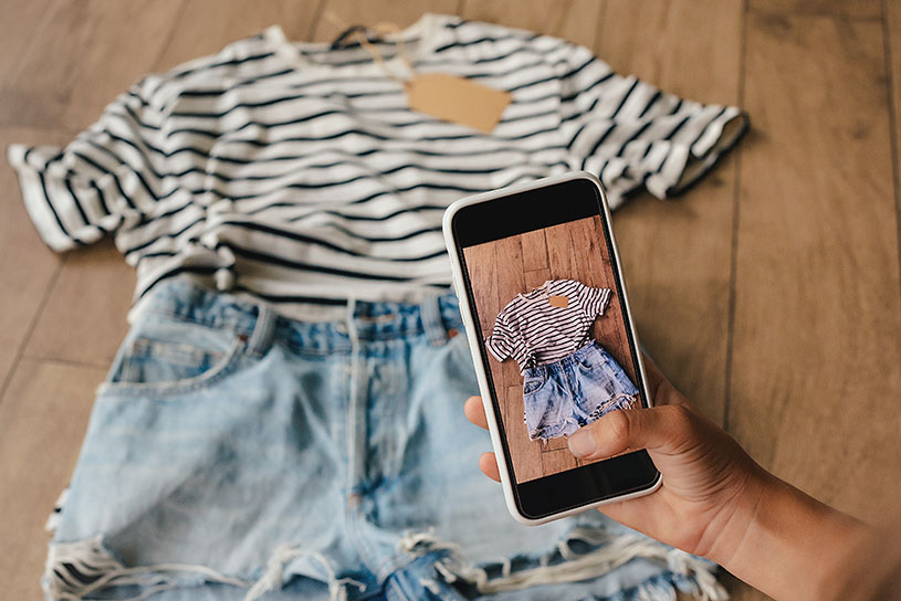 A hand holding a phone and taking a photo of clothes to sell on Vinted