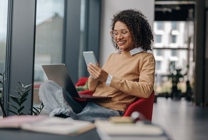 Happy business owner looking at phone and laptop