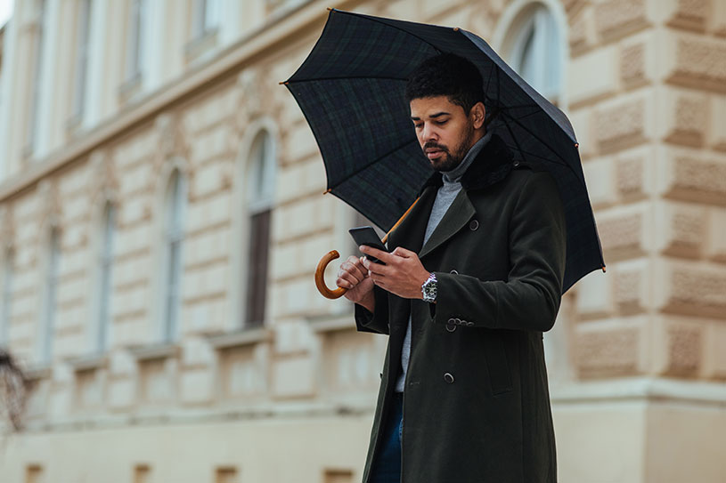 A freelancer checks work on their phone while holding an umbrella