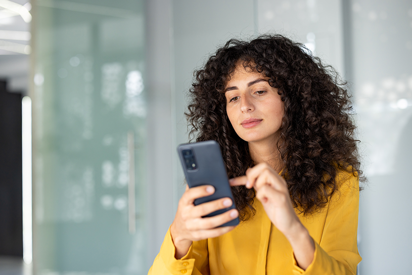 Woman in yellow shirt looks at mobile phone in a concerned way