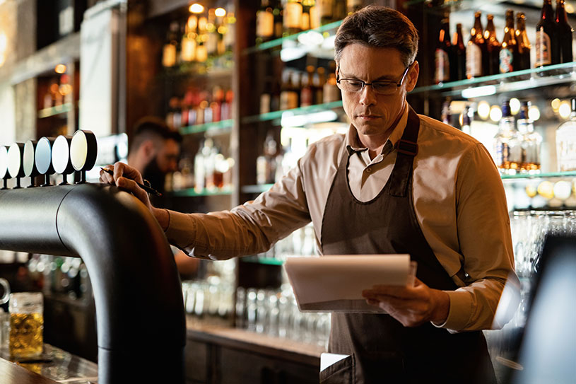 Pub landlord reading inventory behind bar