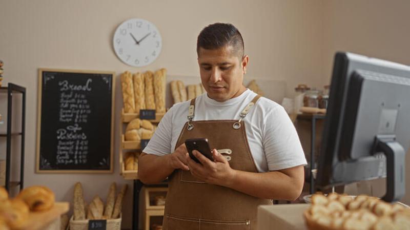 A small business owner looks at their phone in a bakery