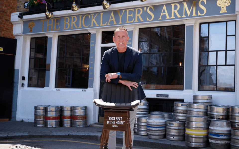Footballer Ray Parlour stands with a pub stool branded with Simply Business's the best seat in the house campaign outside The Bricklayer's Arms in Putney