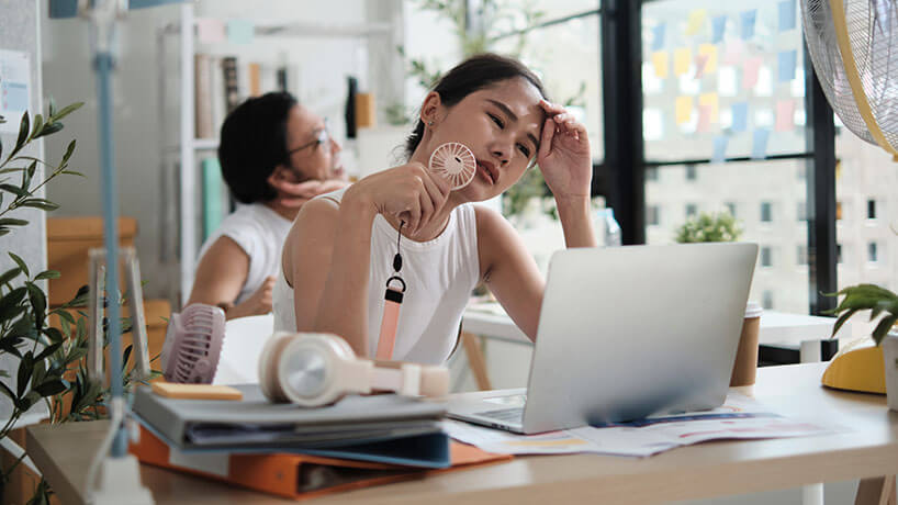 Two workers are unhappy working with hot temperatures at small business office in summer season, uncomfortable with no air conditioner, using fans